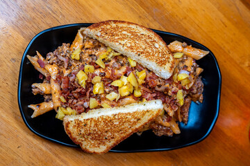 Loaded fries topped with bacon bits, diced yellow peppers and toasted sandwich halves in a black bowl