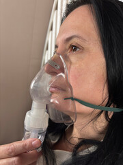Adult woman using a home nebulizer inhaler while sitting in a cozy bedroom, respiratory treatment at home for breathing relief, healthcare and medical therapy concept, realistic lifestyle scene