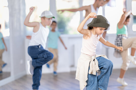 Emotional tween girl mastering krump dance routines during lively group session in children dance studio, guided by passionate male teacher..