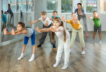 Obraz premium Group of boys and girls with teacher doing warm-up exercises before dancing in studio