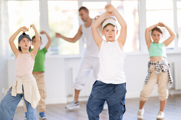 Young happy boy and group of positive children practicing energetic hip hop movements at modern dance school