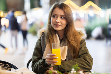 On winter outside of cafe, girl is relaxing at table, drinking juice. Sphere of catering and entertainment for comfort of inhabitants of metropolis, X mas atmosphere. .