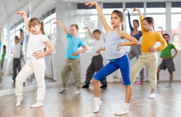 Active preteen girl practicing sport dances with other children and teacher during dancing classes