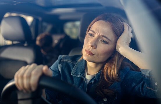 Woman sits in car looking worried and tired
