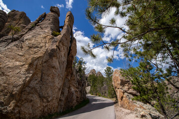 A scenic view along Needles Highway in South Dakota showing the rock formations against a blue sky with white clouds.