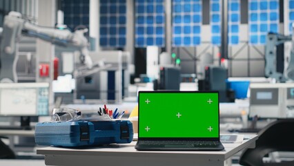 Futuristic solar panel production facility with copy space on empty desk, protective gear and laptop display shows photovoltaic performance. Manufacturing progress and automation.