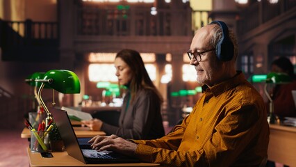 Aged adult disturbing the other people in the library with his music noise, listening to loud music and singing at the desk. Senior man breaking library rules with groovy songs.
