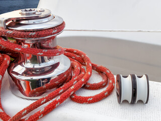 A double sheet block lying next to a winch of a sailboat, with a red main sheet line