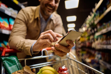 Close up of man using cell phone while shopping at supermarket.