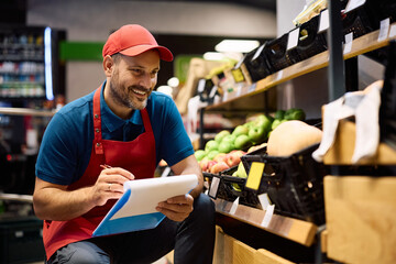 Supermarket worker writing on clipboard while checking stock of fresh groceries at store.