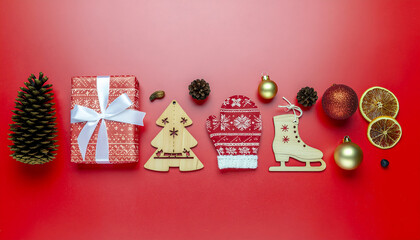 Flat lay of Christmas decorations and gifts on a red background, featuring a pinecone, wrapped present, wooden tree, sweater, ice skates, ornaments, and dried orange slices, evoking a merry