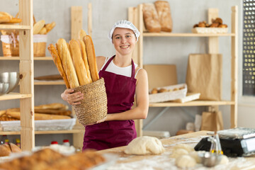 Teenage girl baker posing with basket of homemade baguettes in workshop