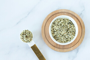Organic hemp seeds in a bowl and spoon on white kitchen table. Top view. Copy space.
