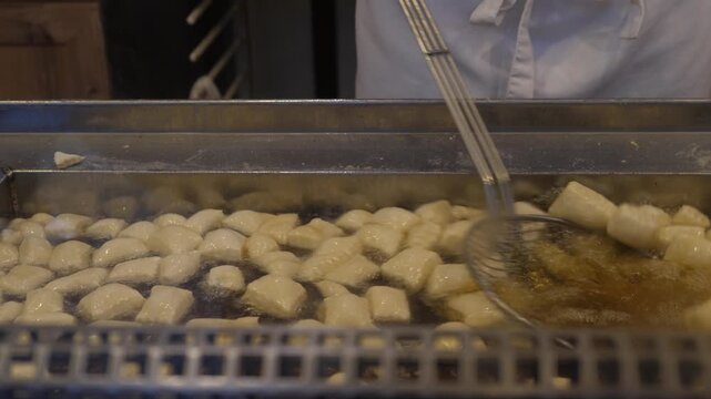 Fresh dough pieces frying in hot oil in a large metal fryer. Close-up shot of traditional street food preparation at a market or festival. The concept of the Christmas market