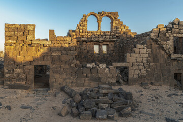 Umm Al-Jimal Sunset: Golden hour on the ancient black basalt ruins in Mafraq, Jordan. Roman tower contrasts with modern cell towers.