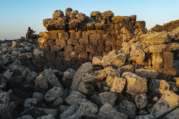 Umm Al-Jimal Sunset: Golden hour on the ancient black basalt ruins in Mafraq, Jordan. Roman tower contrasts with modern cell towers.