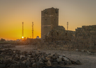 Umm Al-Jimal Sunset: Golden hour on the ancient black basalt ruins in Mafraq, Jordan. Roman tower contrasts with modern cell towers.
