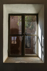 Window in Azraq's old hospital: Sunlight through historic wood frame set in thick stone walls of the black basalt structure in Jordan.