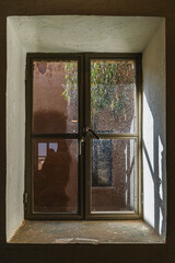 Window in Azraq's old hospital: Sunlight through historic wood frame set in thick stone walls of the black basalt structure in Jordan.