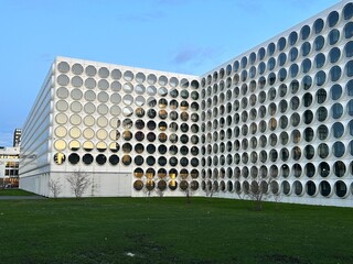 Building with Circular Window Grid in Urban Green Space in Amsterdam. Unique architecture with round glass windows forming a grid pattern on white facade beside green lawn.