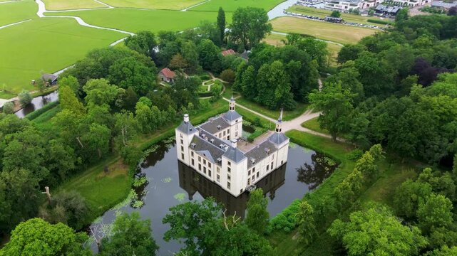 Aerial view of historic castle with four towers, lily filled moat, bridge, and lush gardens harmonious blend of architecture, water, and greenery in a serene heritage setting.