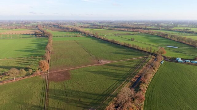 Aerial view of rural fields with crop rows, tree shadows, canal, and farm buildings sunlit landscape blending agriculture, infrastructure, and natural geometry.