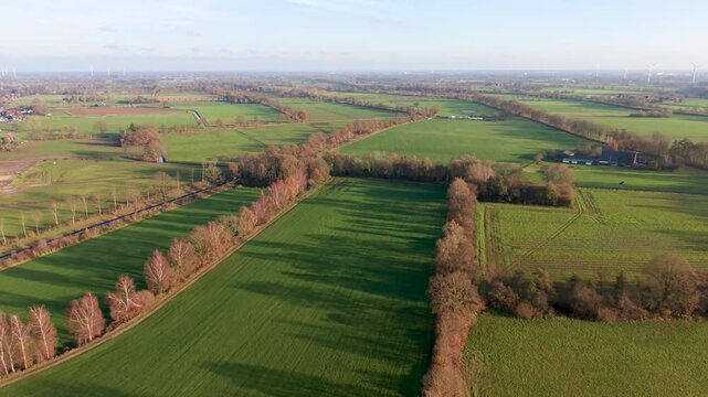 Aerial view of rural fields with crop rows, tree shadows, canal, and farm buildings sunlit landscape blending agriculture, infrastructure, and natural geometry.