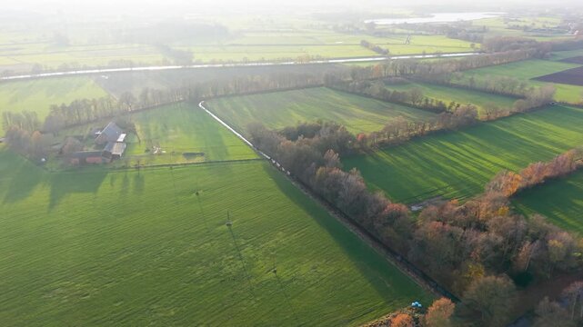 Aerial view of rural fields with crop rows, tree shadows, canal, and farm buildings sunlit landscape blending agriculture, infrastructure, and natural geometry.