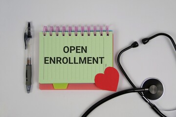 A medical-themed open enrollment concept featuring a notebook labeled 'Open Enrollment', a stethoscope, pen, and a red heart on a white backdrop, symbolizing health care choices.