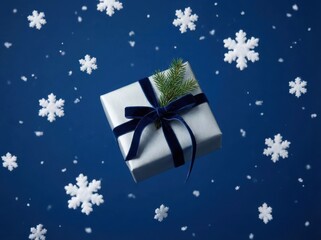 A festive white present is suspended mid-air, surrounded by falling white snowflakes in a high-contrast studio shot against a deep blue background.