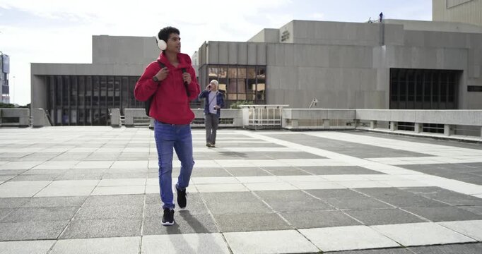 Man in red hoodie walking roof plaza with beeping watch wearing headset checking time calling phone