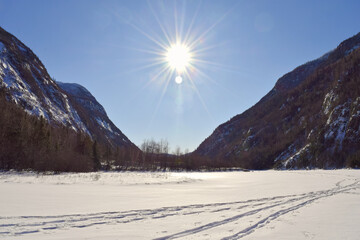 Snowmobile trail on a frozen river surrounded by high mountains on a beautiful winter day