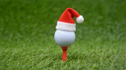 Festive golf- A golf ball wearing a Santa hat rests on a red tee amidst lush green grass,