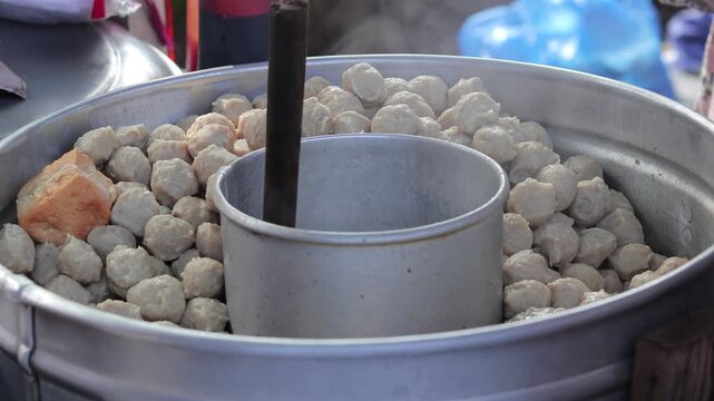 Close up of traditional Indonesian Bakso meatballs and tahu steaming in a large metal pot at a street vendor stall