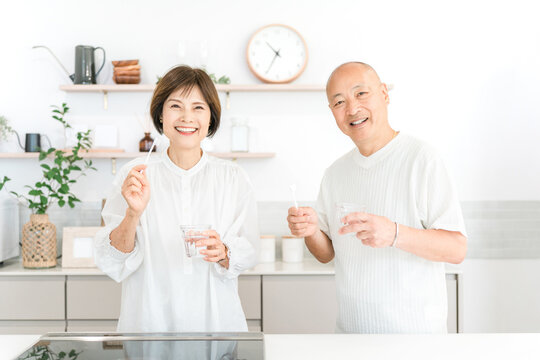 Senior couple brushing their teeth in the kitchen (dental care, bad breath care)
