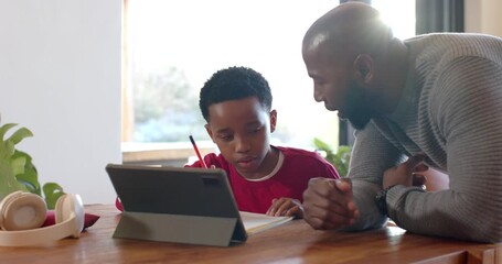 African American father and son doing homework after father pointing at tablet prompt at table - Powered by Adobe