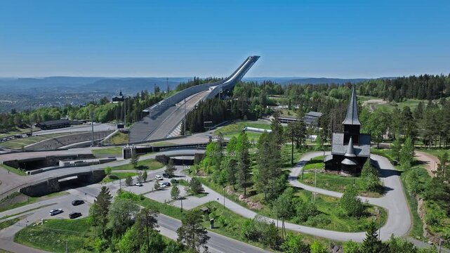 Holmenkollen Ski Stadium 4K Drone Top Angle, Oslo, Norway. Tourists walking arena paths below the ski jump tower, open sunny day, geometric stadium layout.