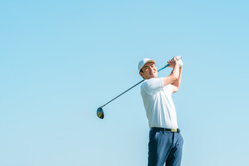 Male golfer swinging a driver at a golf course (blue sky)