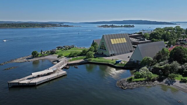 Aerial orbit of Oslo waterfront. Cinematic summer travel drone view capturing museum rooftops, green coast and blue fjord landscape.