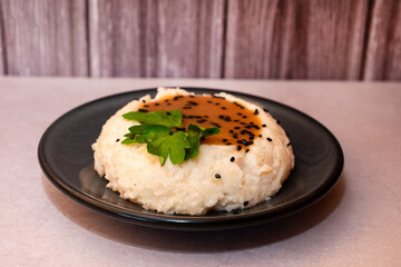 Imagen horizontal de un plato negro con puré de papa y de fondo tablas de madera