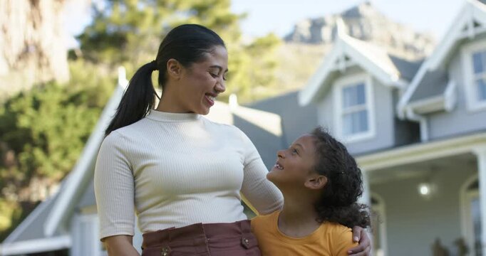African American mother and daughter guiding gaze toward camera then sharing laughter yard by house
