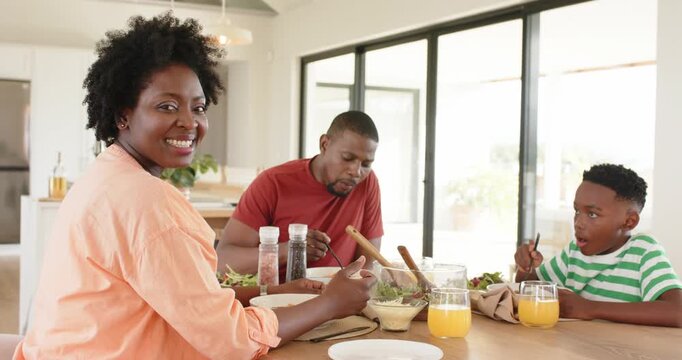 African American family reaching for utensils, eating salad, mother smiling at camera to share joy