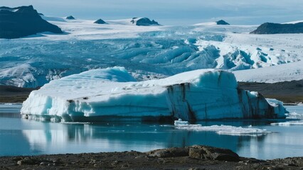 A large iceberg floats in calm glacial waters with a backdrop of snow-covered mountains and ice fields.