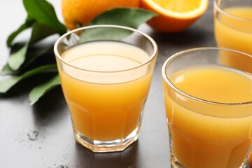 Fresh orange juice, fruits and leaves on grey table, closeup