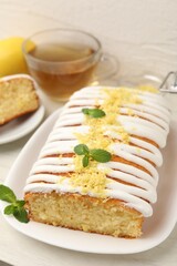 Tasty lemon cake decorated with icing, zest and mint served on white table, closeup