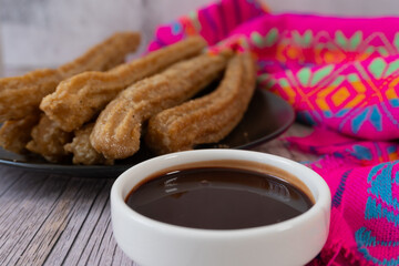 Close-up shot of churros with chocolate on the side, a Mexican dessert, on a wooden table