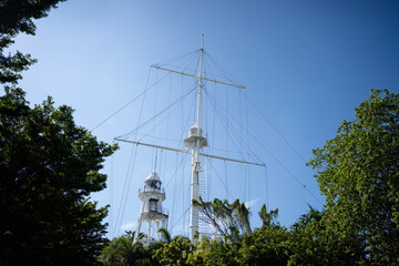 Historic white maritime signal mast with a lighthouse tower surrounded by lush greenery under a clear blue sky.