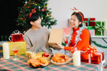 oyful Asian couple exchanging Christmas gifts and celebrating New Year together in a cozy festive setting. happiness, and holiday themes.