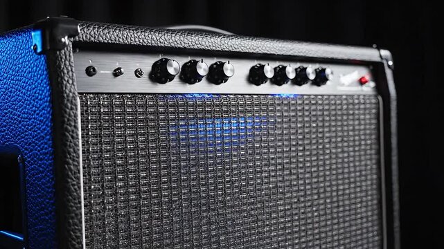Closeup of a black guitar amplifier with knobs and a speaker.