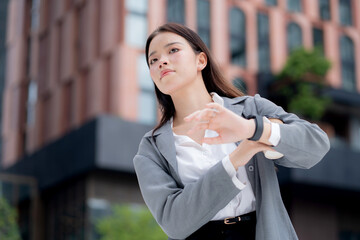 Young asian businesswoman checking time on smartwatch while waiting on busy city street with stress and worried, professional business woman managing schedule and appointment in business district.
